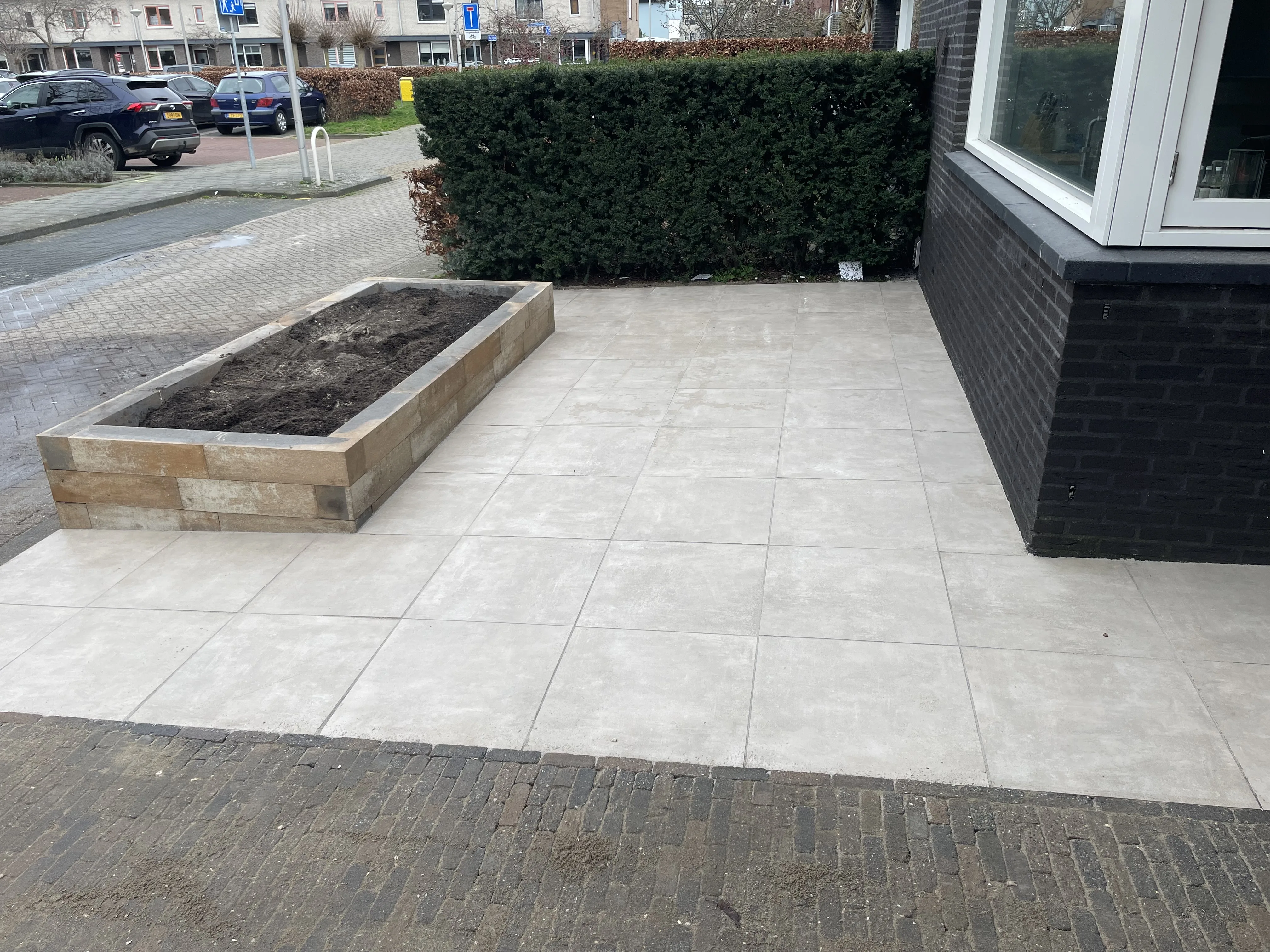 Voortuin renovatie met grote tegels en plantenbak