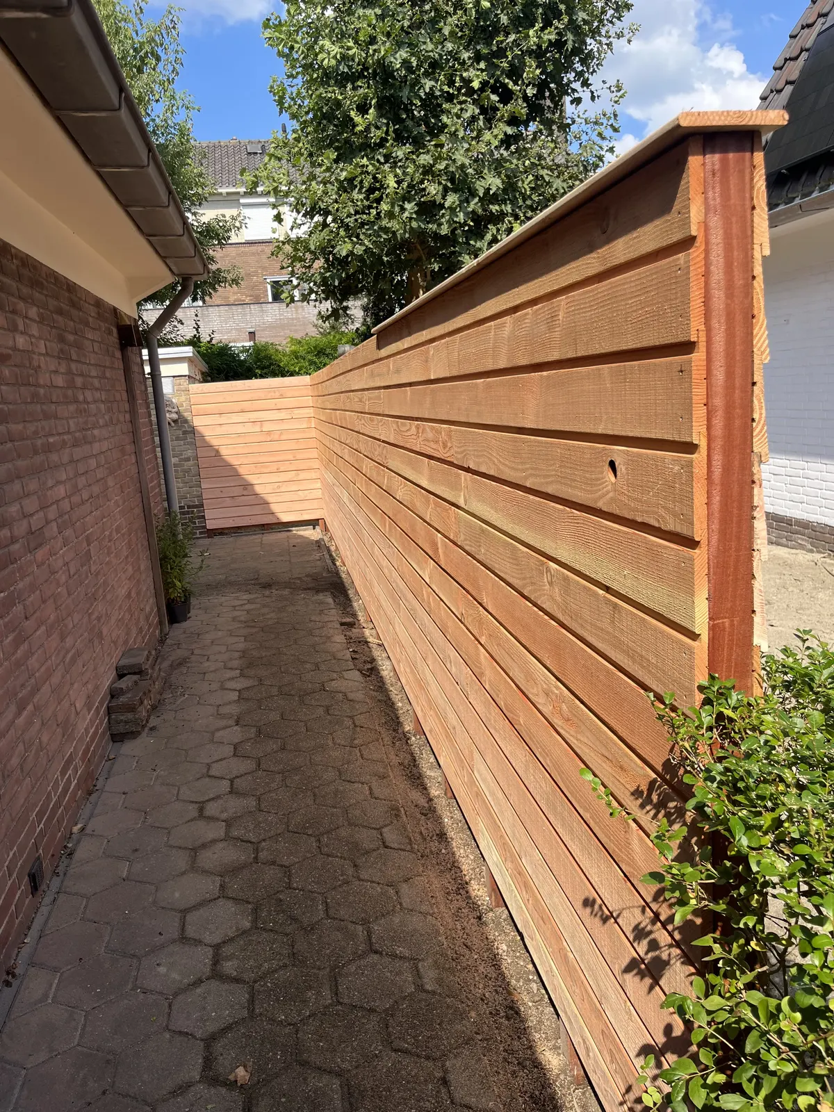Houten schutting naast bestrating – hovenierswerk van Herfst Sierbestrating in Noordeinde